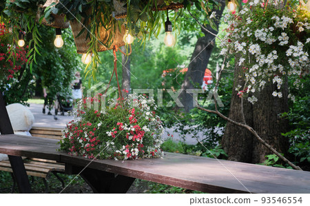 beautiful romantic place at street cafe in a park. wooden table decorated with flowers and wicker baskets. lamps hanging over a table. place for getting rest and dating. beautiful romantic place at street cafe in a park. wooden table decorated with flowers and wicker baskets. lamps hanging over a table. place for getting rest and dating. 93546554