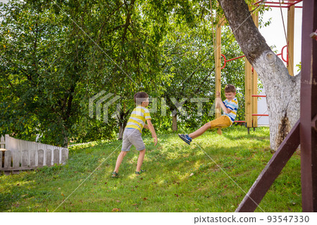 Two adorable happy little boys is having fun on a rope swing which he has found while having rest outside city. Active leisure time with children Two adorable happy little boys is having fun on a rope swing which he has found while having rest outside city. Active leisure time with children 93547330