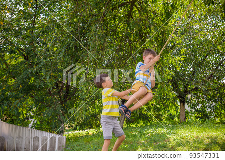 Two adorable happy little boys is having fun on a rope swing which he has found while having rest outside city. Active leisure time with children Two adorable happy little boys is having fun on a rope swing which he has found while having rest outside city. Active leisure time with children 93547331