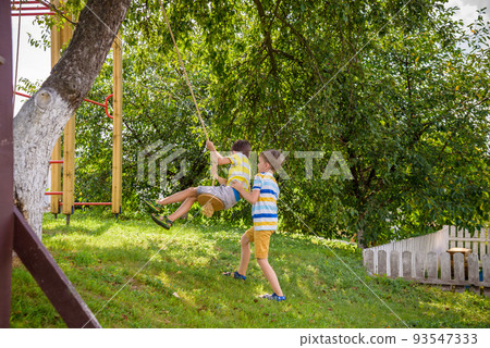 Two adorable happy little boys is having fun on a rope swing which he has found while having rest outside city. Active leisure time with children Two adorable happy little boys is having fun on a rope swing which he has found while having rest outside city. Active leisure time with children 93547333