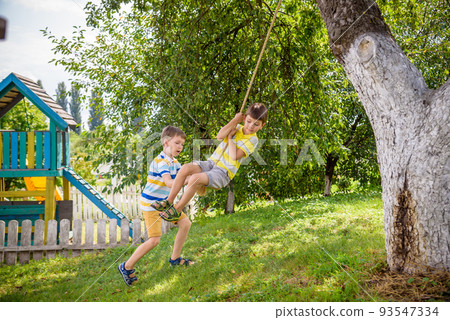 Two adorable happy little boys is having fun on a rope swing which he has found while having rest outside city. Active leisure time with children Two adorable happy little boys is having fun on a rope swing which he has found while having rest outside city. Active leisure time with children 93547334
