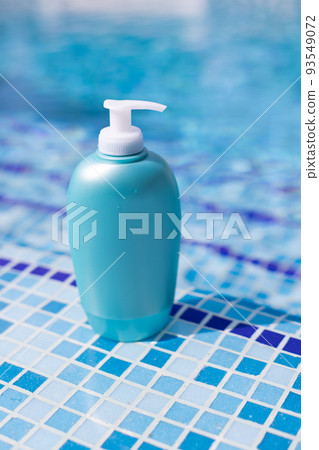 Sunscreen bottle is on steps in blue water of swimming pool. Sunscreen bottle is on steps in blue water of swimming pool. 93549072