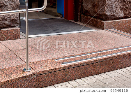 entrance with granite threshold with non-slip rubber and handrail to shop from pedestrian sidewalk through on rubber footmat through glass door, stone facade of building closeup architecture, nobody. 93549116