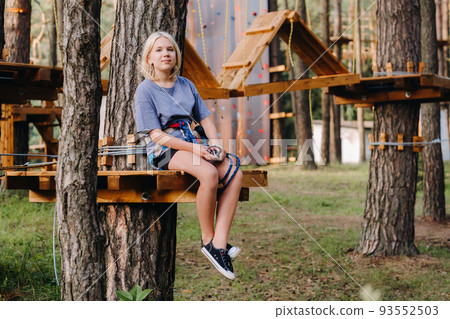 A girl passes an obstacle in a rope town. A girl in a forest rope park A girl passes an obstacle in a rope town. A girl in a forest rope park 93552503