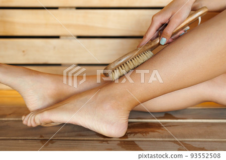 Close-up of woman's legs doing massage with dry wooden brush during spa treatments Close-up of woman's legs doing massage with dry wooden brush during spa treatments 93552508
