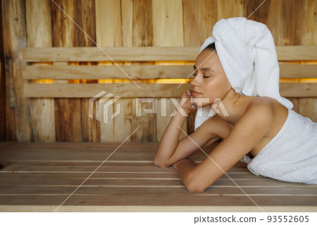 Young woman in white towel lying in wooden sauna Young woman in white towel lying in wooden sauna 93552605