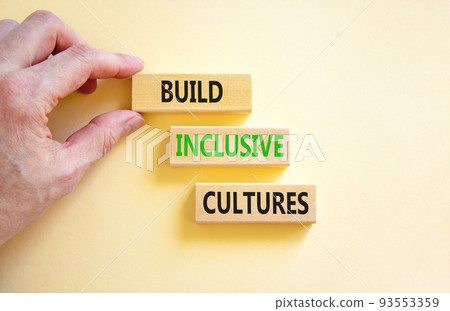Build inclusive cultures symbol. Concept words Build inclusive cultures on wooden blocks. Businessman hand. Beautiful white background. Business build inclusive cultures concept. Copy space. 93553359