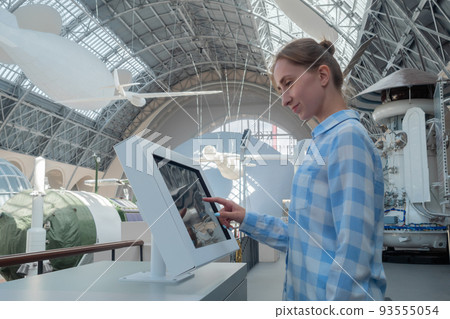 Side view: woman touching interactive touchscreen display kiosk at exhibition 93555054