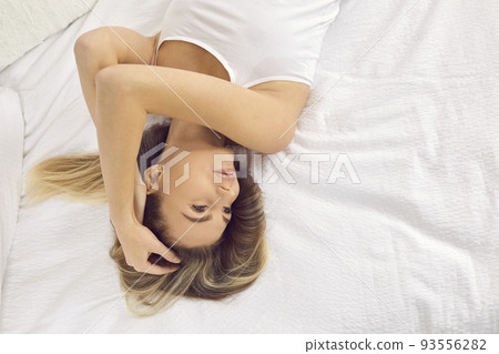 Beautiful young woman in morning relaxes and rests lying on bed with clean white bedding. 93556282