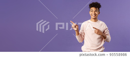 Portrait of enthusiastic, good-looking hispanic man with dreads, looking and pointing upper left corner with satisfied beaming smile, seeing cool thing, made his choice, purple background 93558986