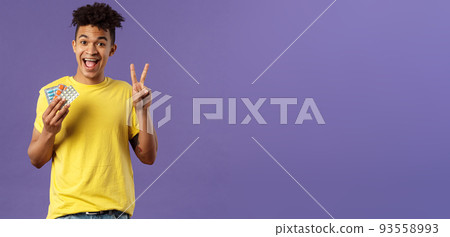 Health, influenza, covid-19 concept. Portrait of upbeat, healthy young man feel much better after taking vitamins or tablets, hold prescribed drugs, show peace sign, smiling pleased 93558993