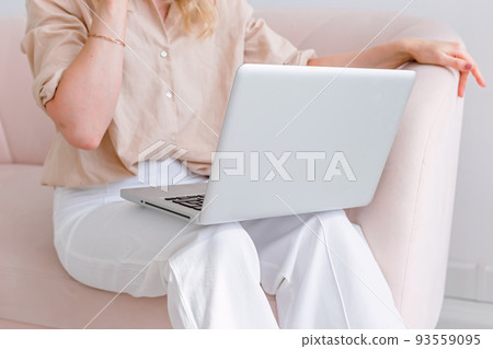Business woman in light clothes, sitting on a sofa, with a open laptop on her knees 93559095