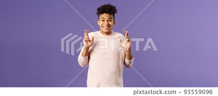 Portrait of hopeful positive, smiling young man having faith in dreams may come true, make wish, cross fingers good luck and awaiting for miracle, standing purple background praying 93559096