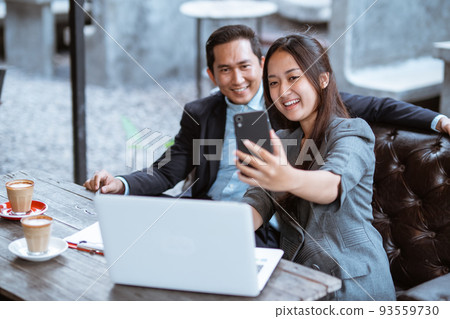 business couple taking a photo of herself using smartphone business couple taking a photo of herself using smartphone 93559730