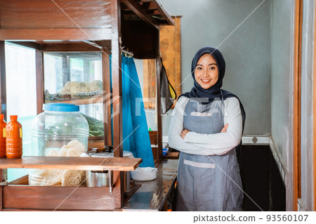 hijab woman wearing apron smiling while standing with crossed hands 93560107