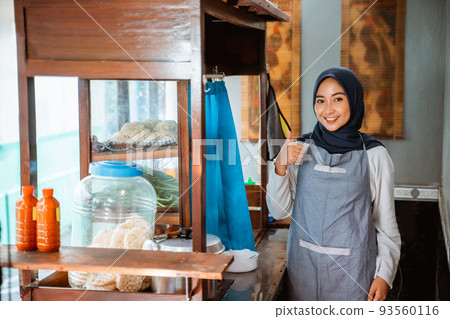 hijab woman wearing apron smiling while standing with thumbs up hijab woman wearing apron smiling while standing with thumbs up 93560116