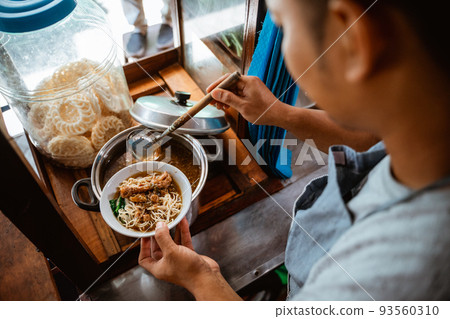 man seller put chicken topping over noodles in a bowl 93560310