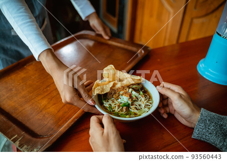 waiter's hand serving a bowl of chicken noodle dish 93560443