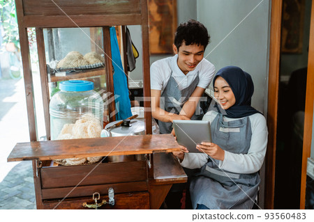 two sellers wearing aprons using pads when selling chicken noodles 93560483