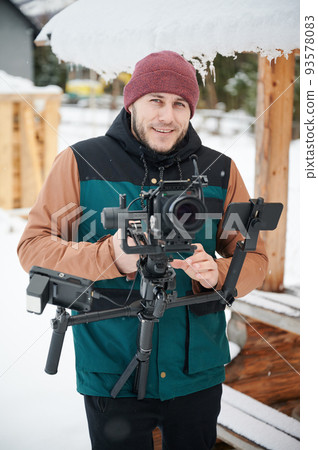 Portrait of happy videographer man shooting footage, using camera mounted on gimbal stabilizer equipment in winter. 93578083