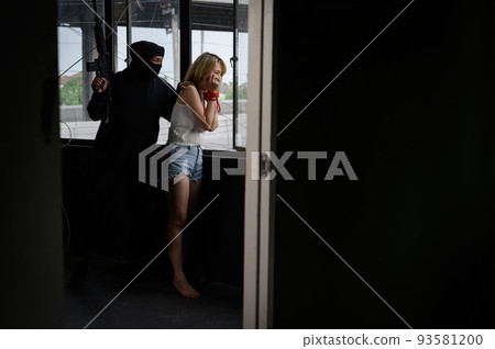 Kidnapper with gun and woman standing looking out of window in old building 93581200