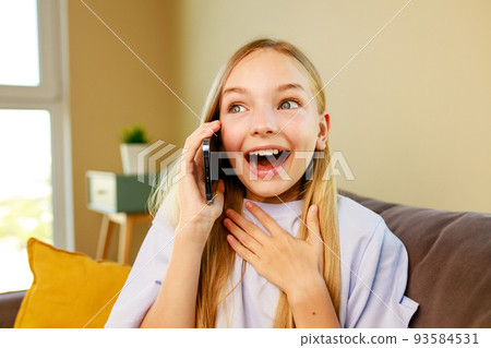 surprised and happy little girl listen great news by phone in cozy living room at home 93584531
