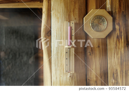Sand timer and thermometer with hygrometer hanging on the wooden wall of the sauna 93584572