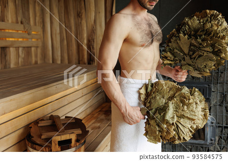 Man with leaf broom in sauna 93584575