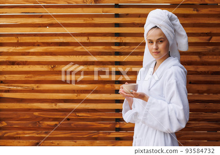 Girl in a bathrobe and a towel wrapped on her head enjoys fragrant tea in the morning Girl in a bathrobe and a towel wrapped on her head enjoys fragrant tea in the morning 93584732