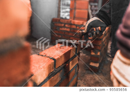 Bricklayer puts bricks to make a wall. 93585656