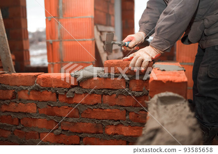 Bricklayer puts bricks to make a wall. 93585658