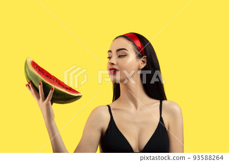 Photo of a beautiful woman with a watermelon posing on a yellow background. 93588264