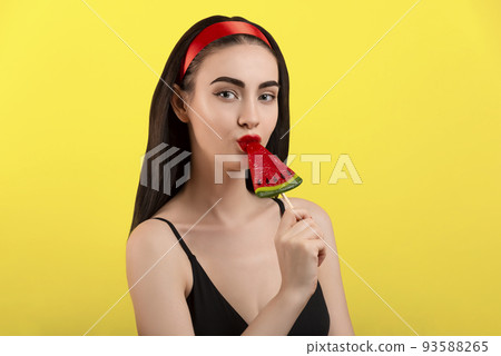 Photo of a beautiful woman with a watermelon on a stick posing on a yellow background. Photo of a beautiful woman with a watermelon on a stick posing on a yellow background. 93588265