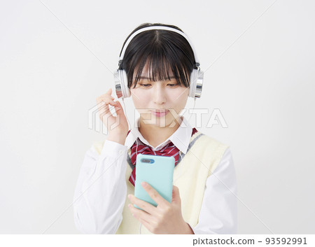 高中女生戴著耳機聽音樂，手持白色背景的智能手機 93592991