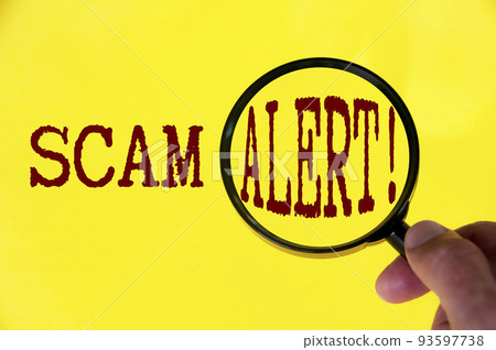 Scam alert text on yellow cover with hand holding magnifying glass. Scamming and fraud concept 93597738