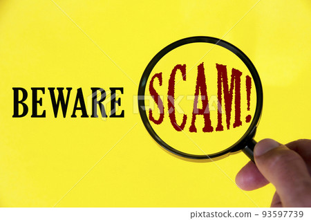 Beware scam text on yellow cover with hand holding magnifying glass. Scamming and fraud concept 93597739