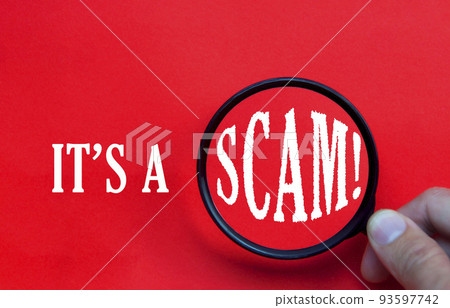 It's a scam text on red cover with hand holding magnifying glass. Scamming and fraud concept. It's a scam text on red cover with hand holding magnifying glass. Scamming and fraud concept. 93597742