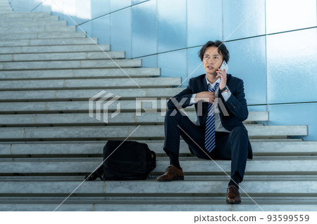 An office worker sitting on the stairs and talking on a smartphone An office worker sitting on the stairs and talking on a smartphone 93599559