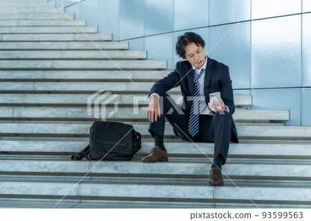 An office worker sitting on the stairs and looking at a smartphone An office worker sitting on the stairs and looking at a smartphone 93599563