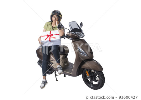 Asian woman with a helmet sitting on a scooter and carrying a gift box Asian woman with a helmet sitting on a scooter and carrying a gift box 93600427