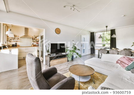 Contemporary minimalist style interior design of light studio apartment with wooden table and chairs in dining zone between open kitchen and living room with white walls and parquet floor 93600759