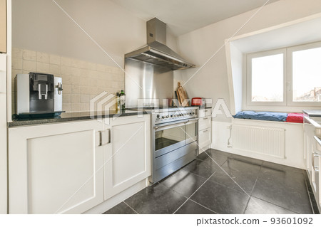 Contemporary cupboards with appliances and tables with kitchenware located in light kitchen near dining room in stylish apartment Contemporary cupboards with appliances and tables with kitchenware located in light kitchen near dining room in stylish apartment 93601092