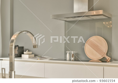 Fragment of interior of light narrow home kitchen with minimalist style white furniture with sink and stove Fragment of interior of light narrow home kitchen with minimalist style white furniture with sink and stove 93601554
