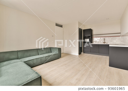 Simple open plan kitchen with white cabinets and living room with gray sofa in daylight 93601965