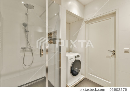 Shower faucets attached to tiled wall near glass partition and washing machine in washroom at home 93602276