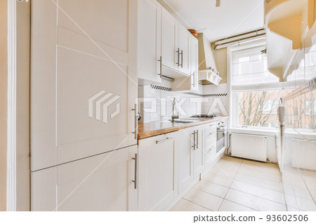 Fragment of interior of light narrow home kitchen with minimalist style white furniture with sink and stove Fragment of interior of light narrow home kitchen with minimalist style white furniture with sink and stove 93602506
