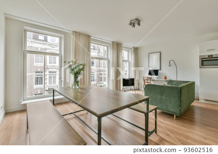 Stylish interior design of living room with light furniture and soft comfy couch and carpet and with pc on cabinet in modern apartment with open kitchen and white walls 93602516