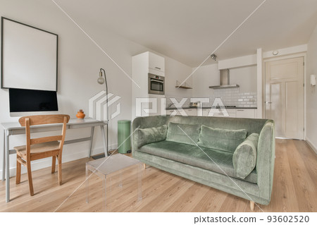 Stylish interior design of living room with light furniture and soft comfy couch and carpet and with pc on cabinet in modern apartment with open kitchen and white walls 93602520