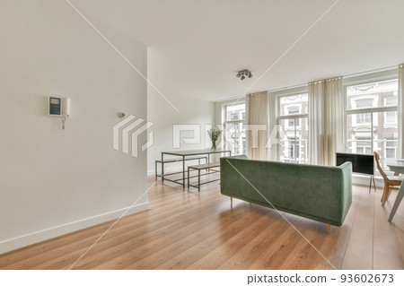 Stylish interior design of living room with light furniture and soft comfy couch and carpet and with pc on cabinet in modern apartment with open kitchen and white walls 93602673