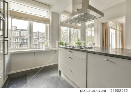 Illuminated cupboards with washbasin and appliances located in spacious light kitchen in contemporary flat 93602985